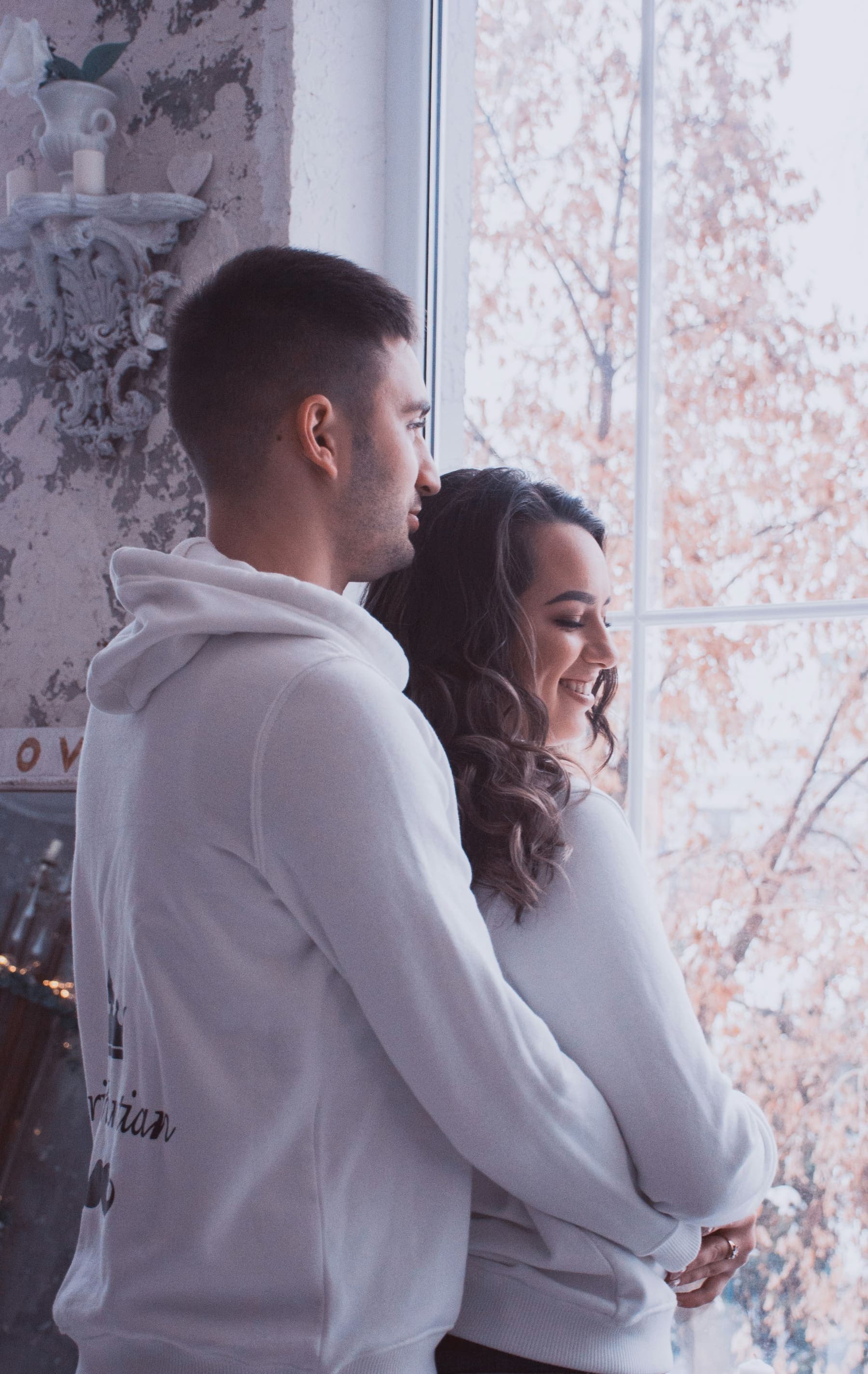 A couple by a window in soft morning light, looking out together